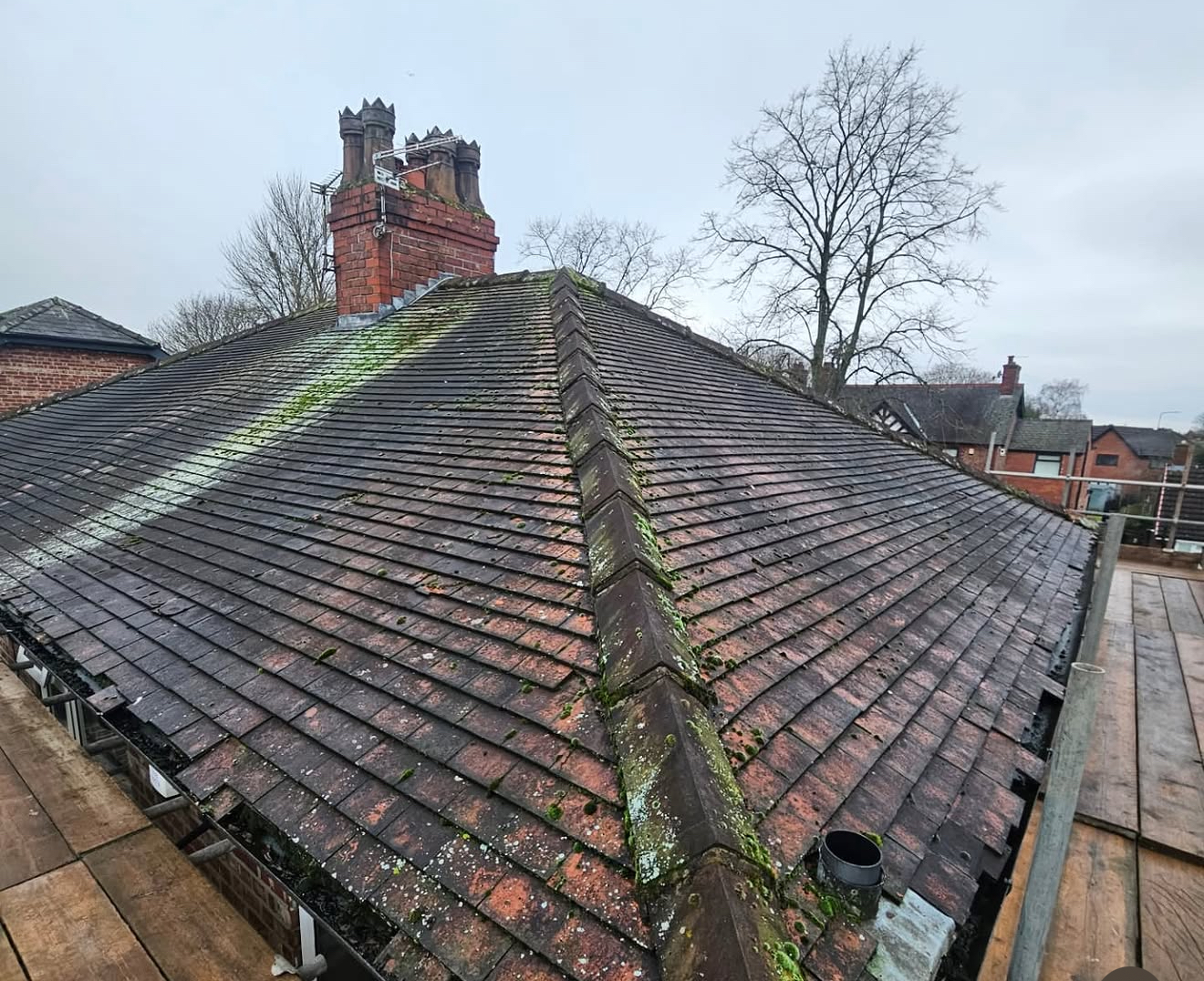Moss-covered and weathered tiled roof with a brick chimney before repair work